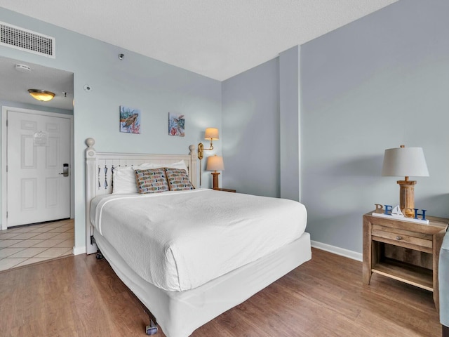 bedroom featuring a textured ceiling, wood finished floors, baseboards, and visible vents