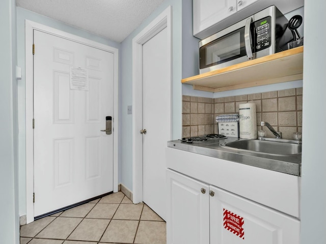 kitchen featuring white cabinets, light tile patterned flooring, stainless steel microwave, a sink, and backsplash