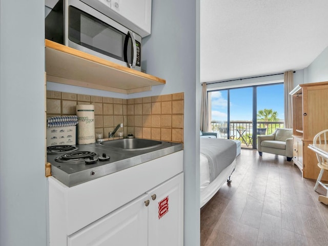 kitchen with tasteful backsplash, white cabinetry, wood finished floors, stainless steel microwave, and a sink
