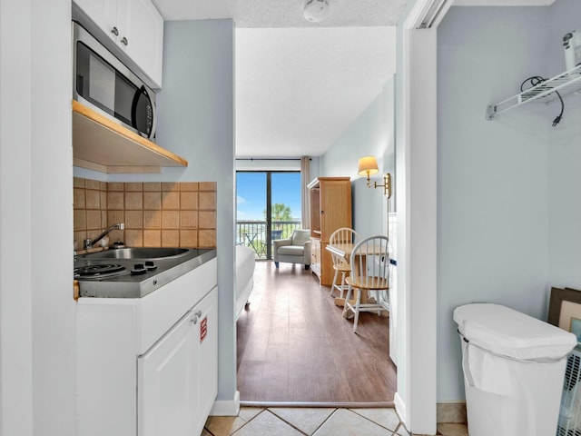 kitchen featuring stainless steel microwave, white cabinets, a sink, and backsplash