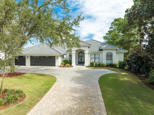 view of front facade featuring a tiled roof, a garage, a front yard, stucco siding, and driveway