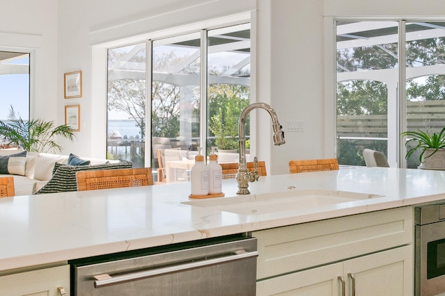 kitchen featuring dishwasher, a sink, and light stone counters