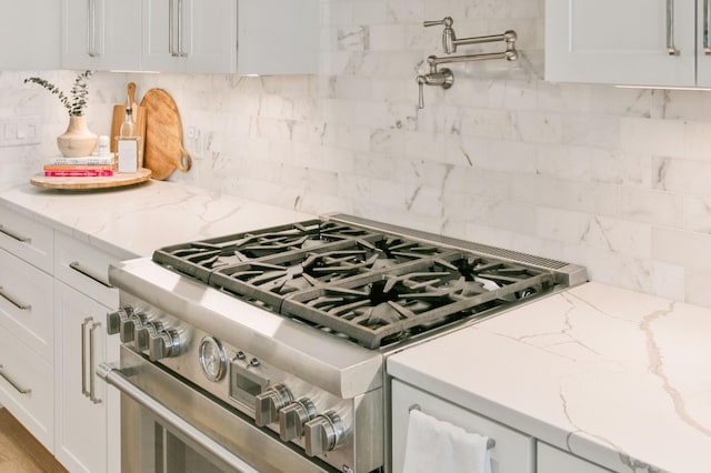 kitchen with white cabinetry, tasteful backsplash, light stone counters, and stainless steel range