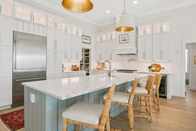 kitchen featuring ornamental molding, stainless steel appliances, a center island with sink, a sink, and beverage cooler