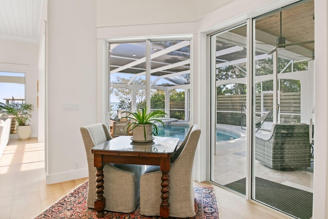 dining space featuring baseboards, a sunroom, a ceiling fan, and light wood finished floors