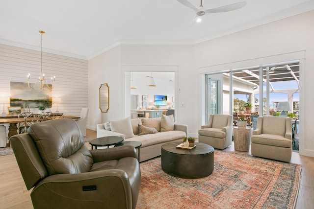 living area with ceiling fan with notable chandelier, crown molding, wood finished floors, and baseboards