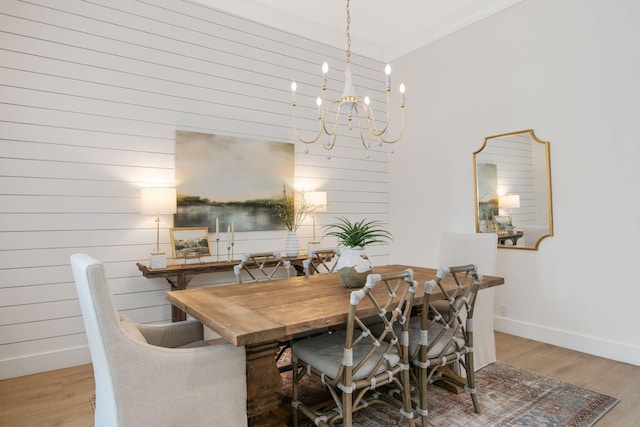 dining space featuring wooden walls, crown molding, baseboards, wood finished floors, and an inviting chandelier
