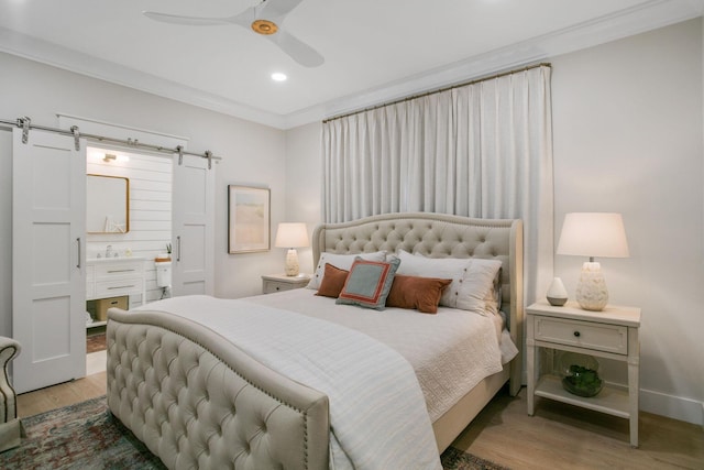 bedroom featuring connected bathroom, crown molding, a barn door, wood finished floors, and recessed lighting