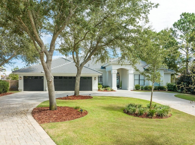 view of front of house with curved driveway, stucco siding, a tiled roof, a front yard, and a garage