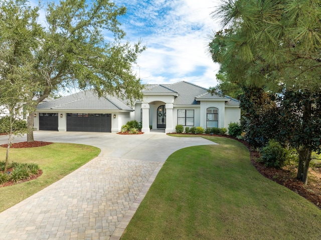view of front of house featuring a tile roof, stucco siding, an attached garage, decorative driveway, and a front yard