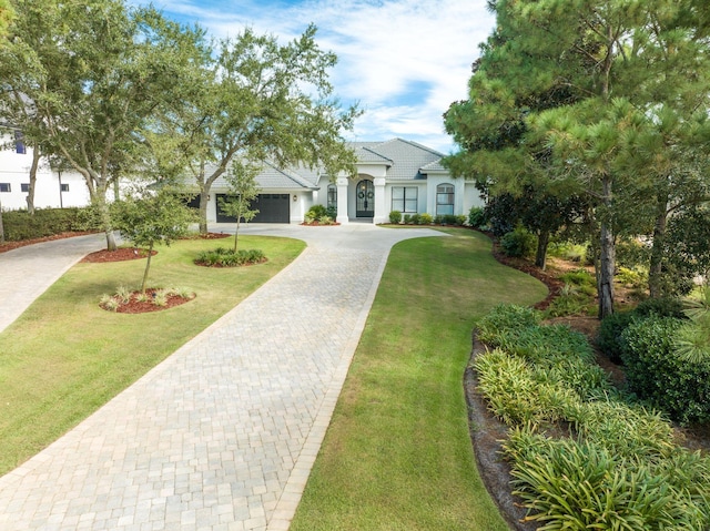 view of front facade with stucco siding, decorative driveway, a garage, and a front lawn