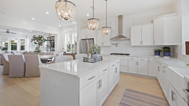 kitchen featuring decorative backsplash, high end fridge, crown molding, a center island, and wall chimney range hood