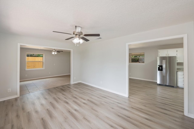 empty room with a healthy amount of sunlight, a ceiling fan, light wood finished floors, and visible vents
