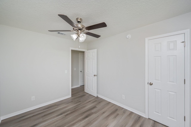 unfurnished bedroom with baseboards, a textured ceiling, wood finished floors, and visible vents
