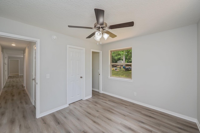 unfurnished bedroom with light wood-style floors, a textured ceiling, baseboards, and ceiling fan