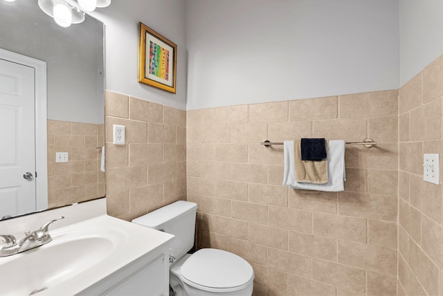half bath featuring vanity, tile walls, toilet, and wainscoting