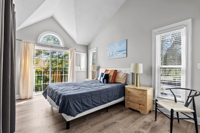 bedroom with access to outside, wood finished floors, a baseboard heating unit, and lofted ceiling