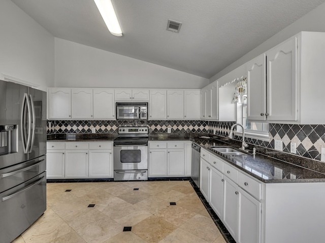 27 Hidden Harbor Ln, Miramar Beach, FL 32550 - kitchen with stainless steel appliances, vaulted ceiling, a sink, white cabinets, and decorative backsplash