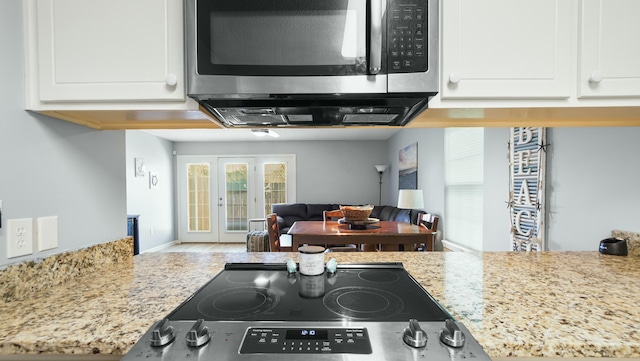 kitchen with stainless steel appliances, light stone countertops, open floor plan, and white cabinets