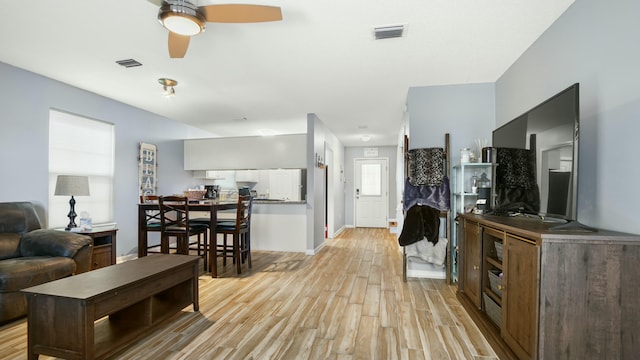 living room featuring light wood finished floors, visible vents, baseboards, and ceiling fan
