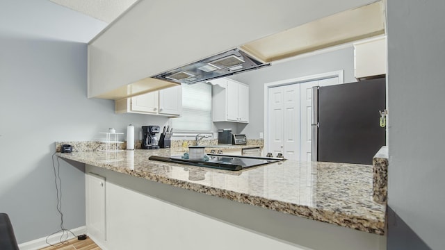kitchen with range hood, freestanding refrigerator, light stone countertops, white cabinets, and black electric cooktop