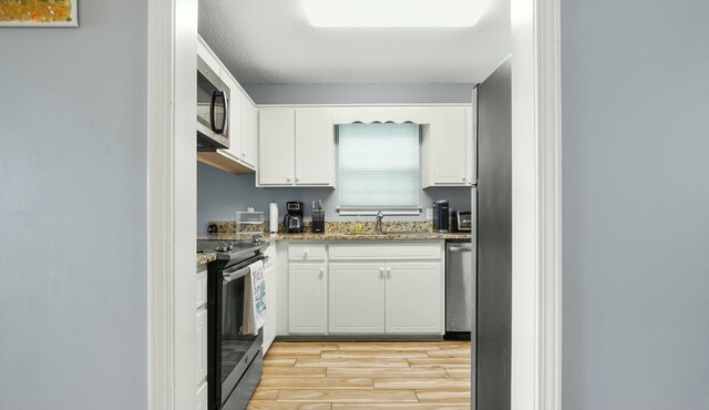 kitchen with white cabinets, a sink, appliances with stainless steel finishes, light wood-style flooring, and light stone counters
