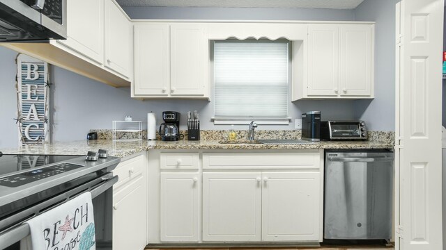 kitchen featuring a sink, appliances with stainless steel finishes, white cabinetry, a toaster, and light stone counters