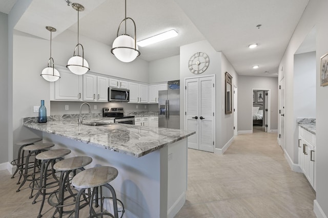 kitchen featuring a sink, a kitchen breakfast bar, a peninsula, light stone countertops, and stainless steel appliances