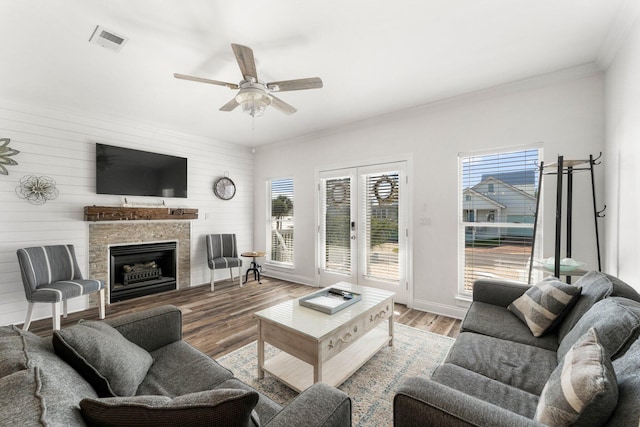 living area featuring visible vents, ornamental molding, ceiling fan, a fireplace, and wood finished floors