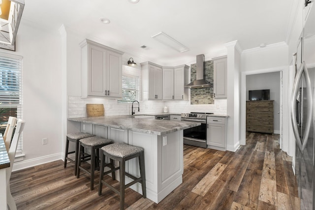 kitchen with tasteful backsplash, a peninsula, wall chimney range hood, appliances with stainless steel finishes, and a sink