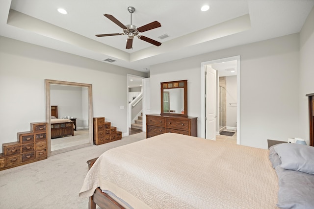 bedroom with a tray ceiling, light carpet, ensuite bathroom, and visible vents