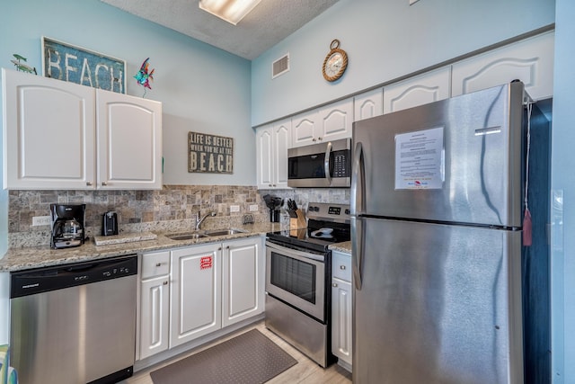 kitchen with white cabinetry, light stone countertops, visible vents, stainless steel appliances, and a sink