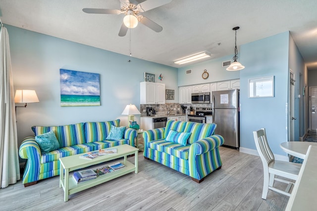 living room with visible vents, light wood-type flooring, baseboards, and ceiling fan