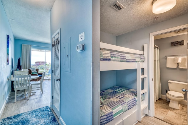 bedroom featuring a textured ceiling, wood finished floors, baseboards, and visible vents