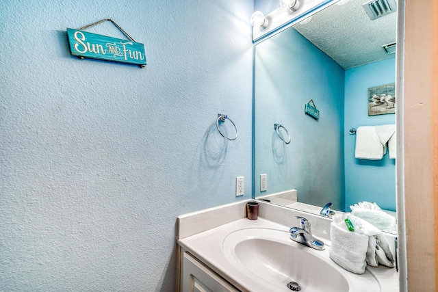 bathroom featuring a textured wall, vanity, visible vents, and a textured ceiling