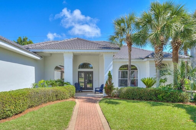 view of exterior entry featuring french doors, a lawn, stucco siding, and a tiled roof