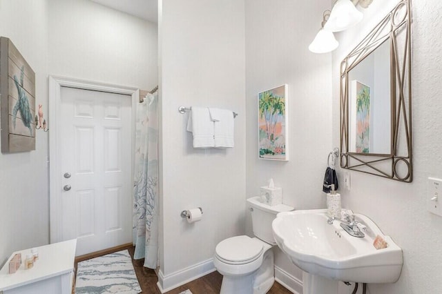 bathroom featuring baseboards, curtained shower, toilet, a sink, and wood finished floors
