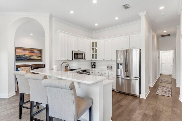 kitchen with glass insert cabinets, tasteful backsplash, a peninsula, stainless steel appliances, and a breakfast bar area