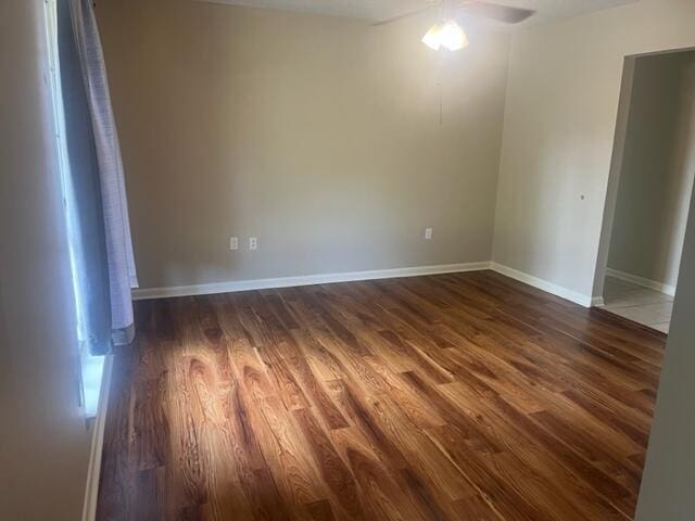 unfurnished room featuring baseboards, a ceiling fan, and dark wood finished floors