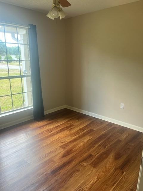 unfurnished room with baseboards, dark wood-style floors, and a healthy amount of sunlight