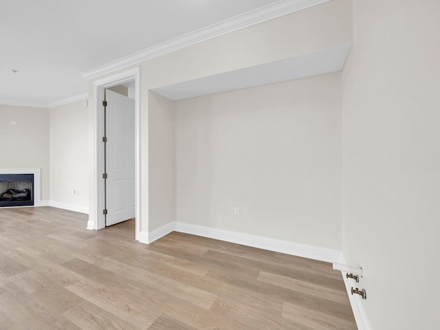 basement featuring a fireplace, light wood-style floors, baseboards, and crown molding