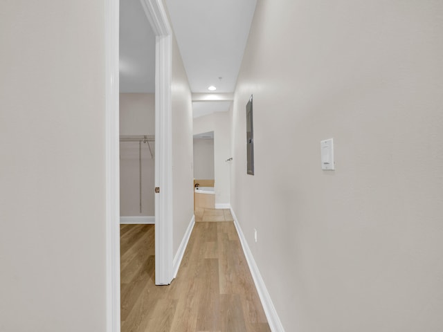 corridor with baseboards, light wood-style floors, and electric panel