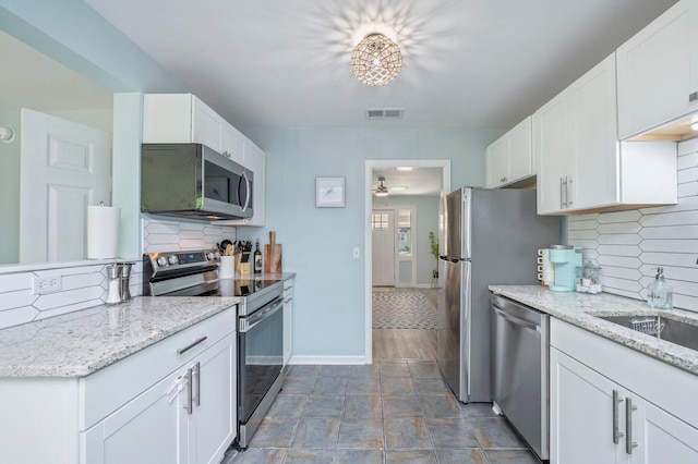 kitchen with appliances with stainless steel finishes, white cabinets, visible vents, ceiling fan, and decorative backsplash