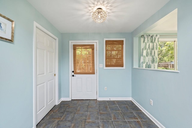 foyer featuring a chandelier, stone finish flooring, baseboards, and plenty of natural light