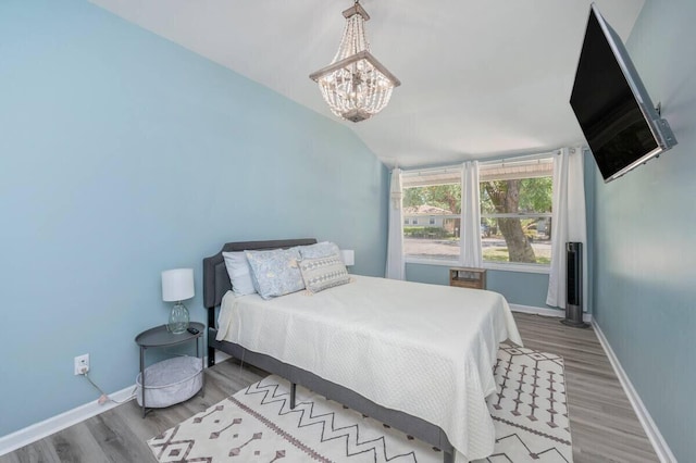 bedroom with baseboards, a chandelier, wood finished floors, and lofted ceiling