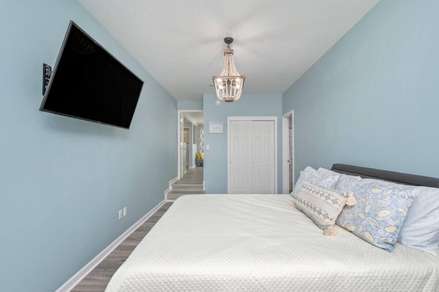 bedroom featuring a closet, baseboards, a chandelier, and wood finished floors