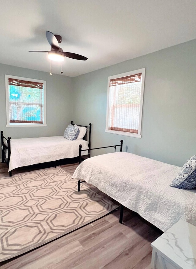 bedroom with ceiling fan, multiple windows, and wood finished floors