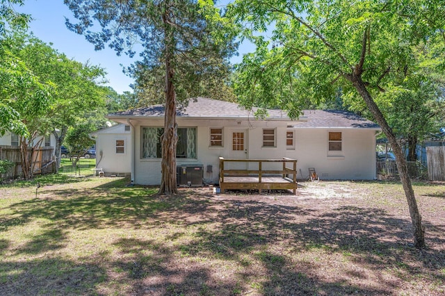 rear view of property with a deck, a lawn, fence, cooling unit, and roof with shingles