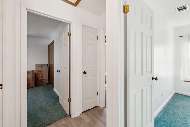 hallway with baseboards, light carpet, a textured ceiling, light wood-style floors, and visible vents