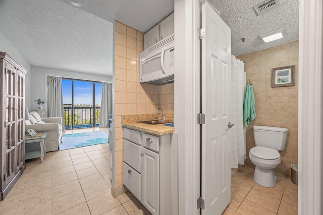 bathroom featuring visible vents, toilet, tile walls, a textured ceiling, and tile patterned flooring